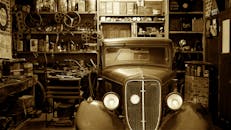 怀旧车间里停着一辆古董汽车，周围摆满了古董工具和零件