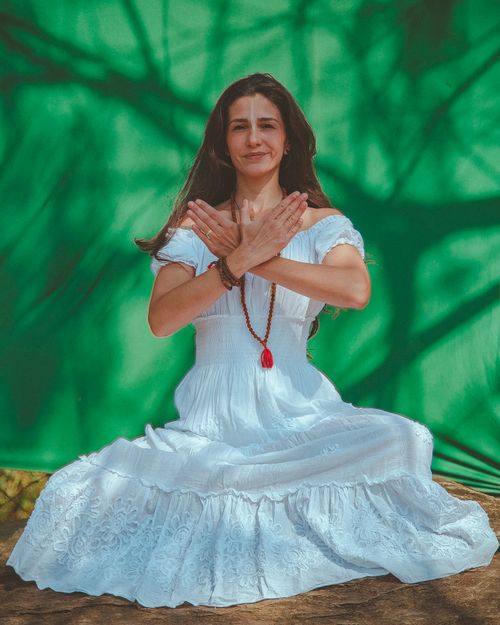 Free A serene woman in a white dress meditating outdoors against a green backdrop. Stock Photo