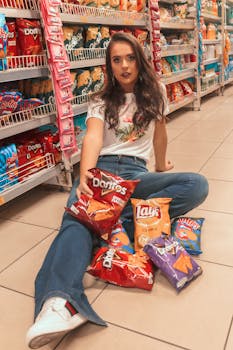 一位时尚的年轻女子坐在超市地板上，周围散落着零食袋