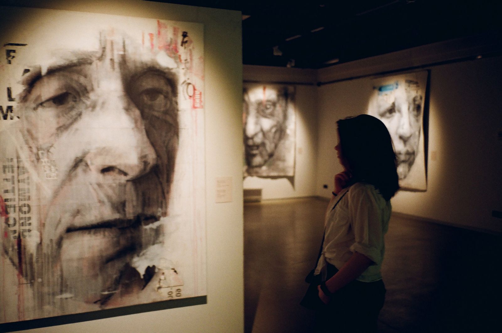 Visitor looking closely at large portrait paintings in a dark gallery