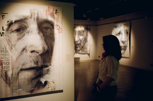 Free A woman observes portrait paintings in a dimly lit modern art gallery. Stock Photo