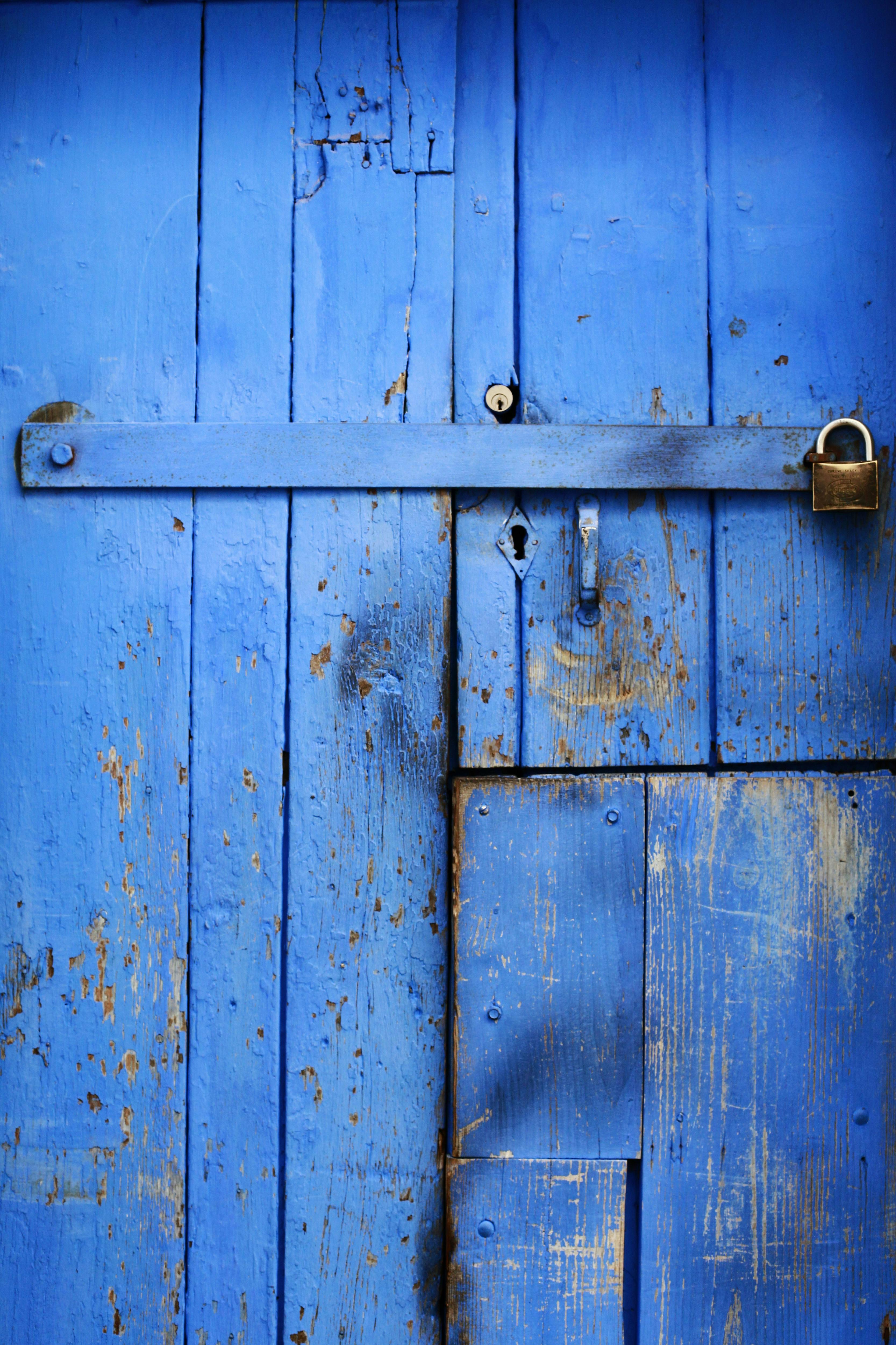 A close-up of a rustic blue wooden door with a metal lock, highlighting texture.