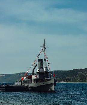 A classic boat adorned with colorful flags on a tranquil lake with scenic hills.