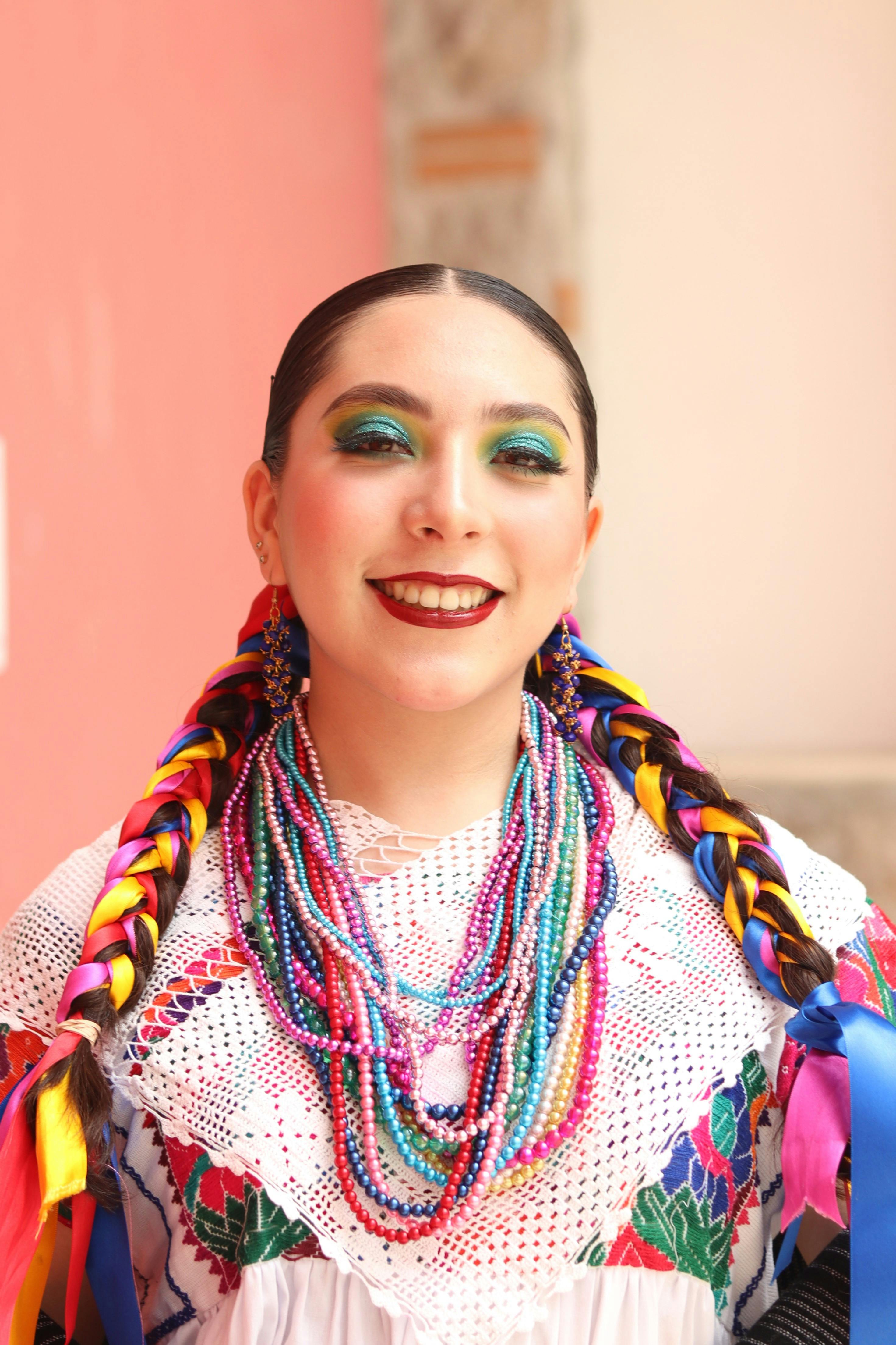 Smiling woman with colorful braids and beads in traditional attire outdoors.
