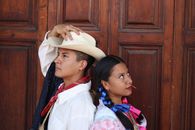 A couple in traditional Mexican attire posing creatively against a wooden background.