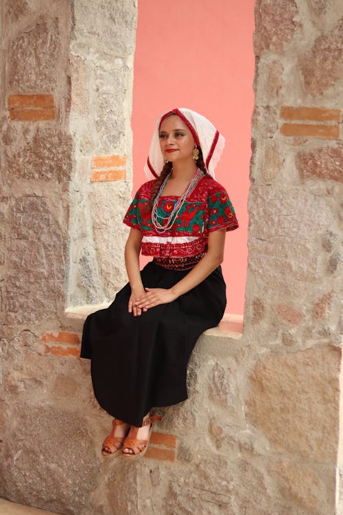 A woman in traditional mexican clothing sitting on a ledge