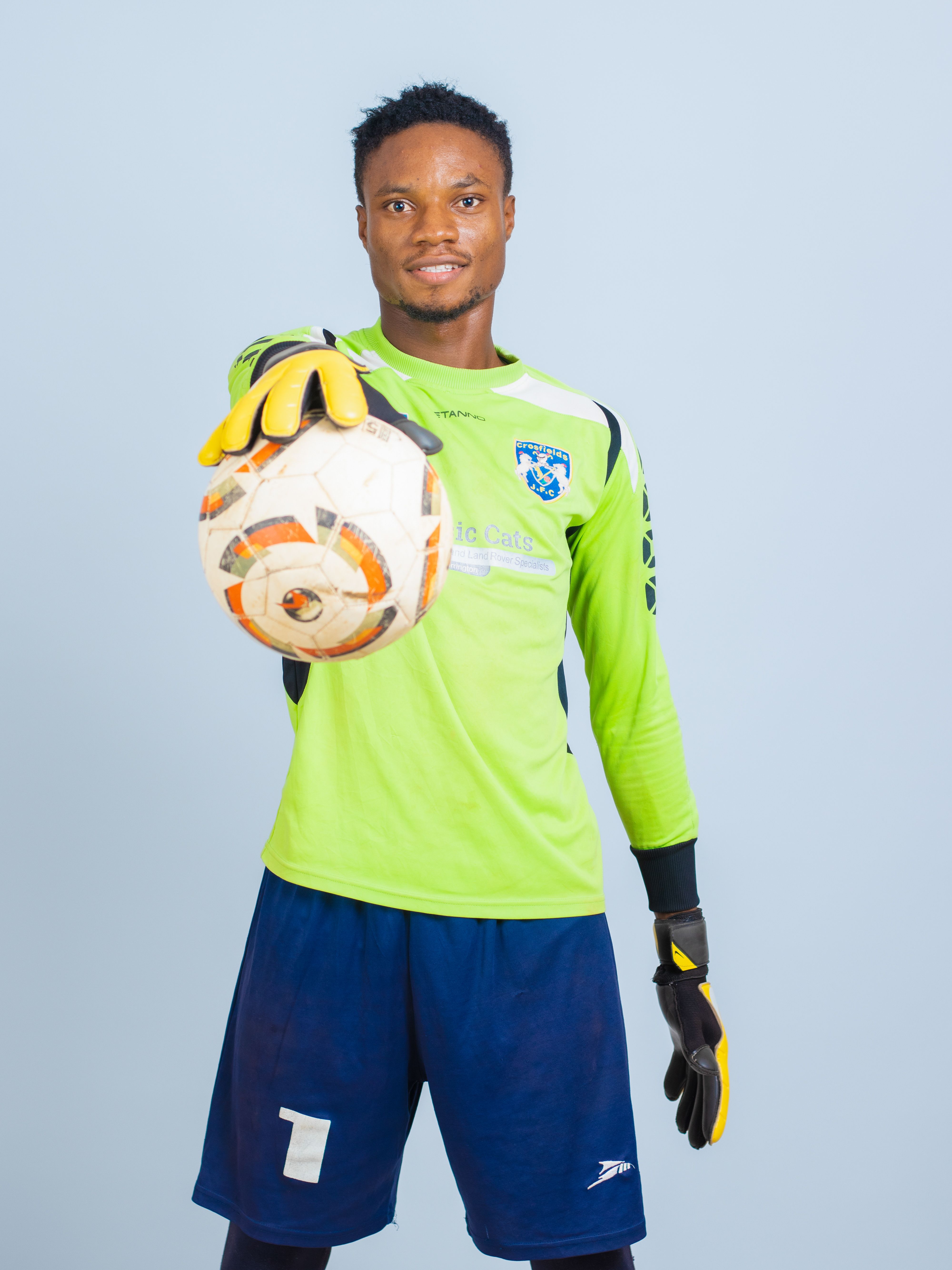 Athlete in soccer gear holding a ball against a light background, showcasing focus.