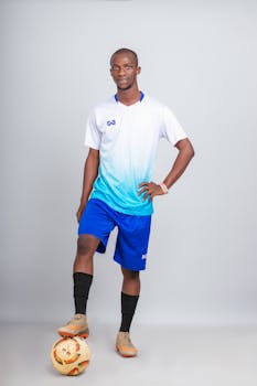 Studio shot of an African male football player posing with a soccer ball on a white background.