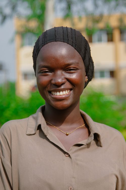 Free Young woman wearing a grey blouse and headscarf, smiling brightly outdoors. Natural light, candid portrait. Stock Photo