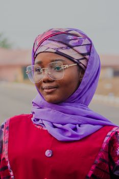 A smiling woman in colorful traditional clothing and glasses outdoors.