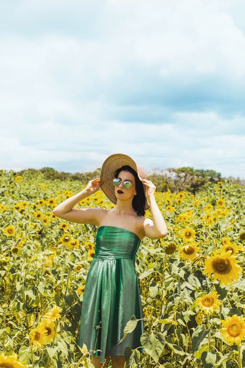 Donna Che Indossa Abito Tubo Verde E Cappello Da Sole In Piedi In Mezzo Al Prato Di Girasole