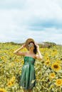 阳光明媚的日子里，一位穿着绿色连衣裙、戴着帽子的时尚女人在充满活力的向日葵地里摆姿势