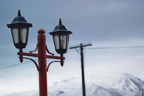 Free A red street lamp set against a snowy mountain backdrop on a cloudy winter day. Stock Photo