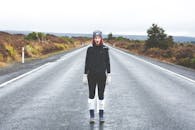 一名穿着冬装的妇女站在乡村道路上，道路潮湿空旷，四周环绕着乡村景色