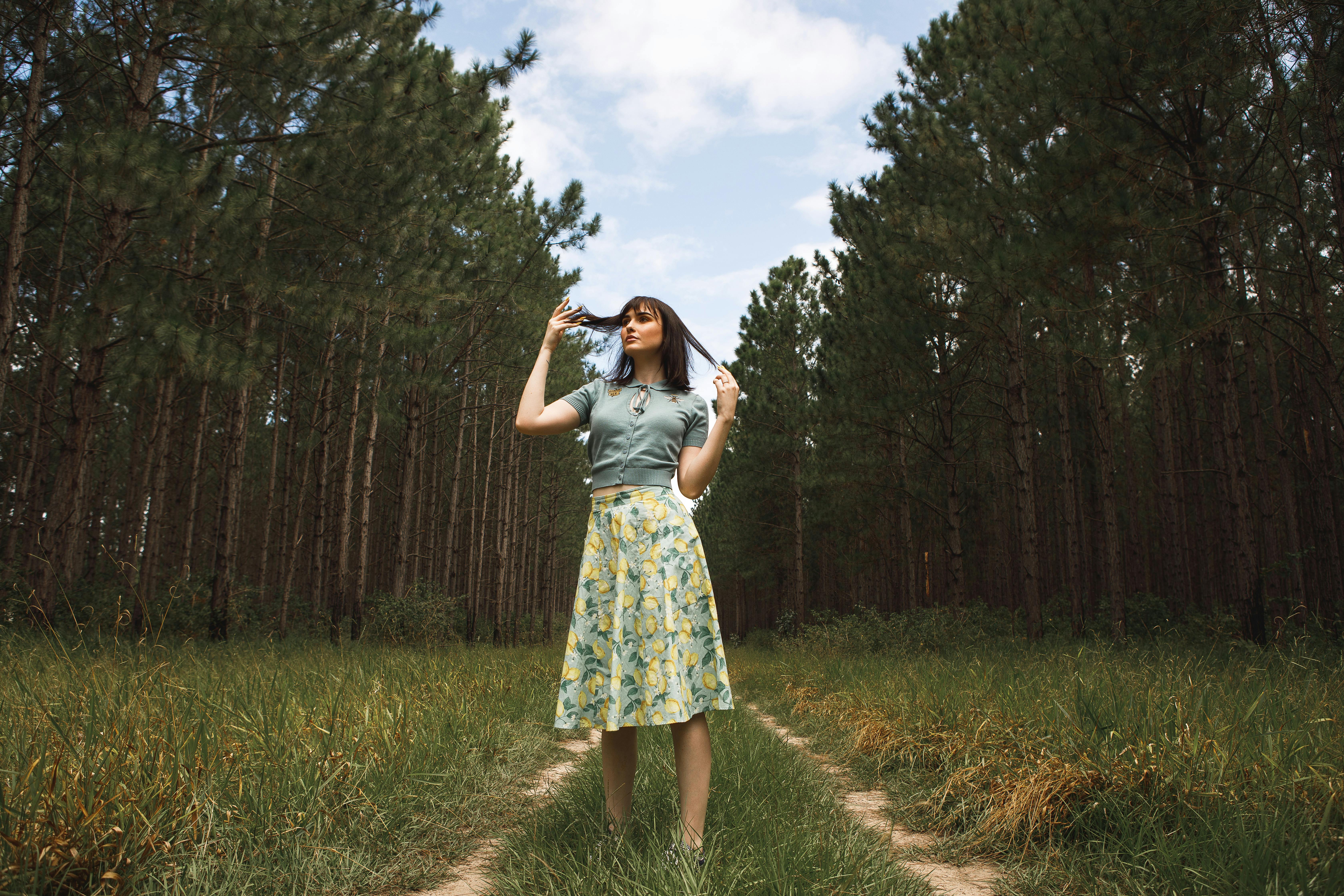 一位穿着花卉裙子的优雅女子，站在绿树环绕的森林小路上