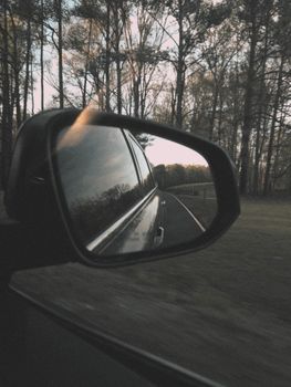 View through car side mirror reflecting a scenic drive through lush forest, capturing nature's tranquility.