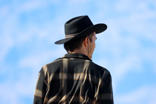 Free Back view of a man wearing a plaid shirt and cowboy hat against a blue sky. Stock Photo