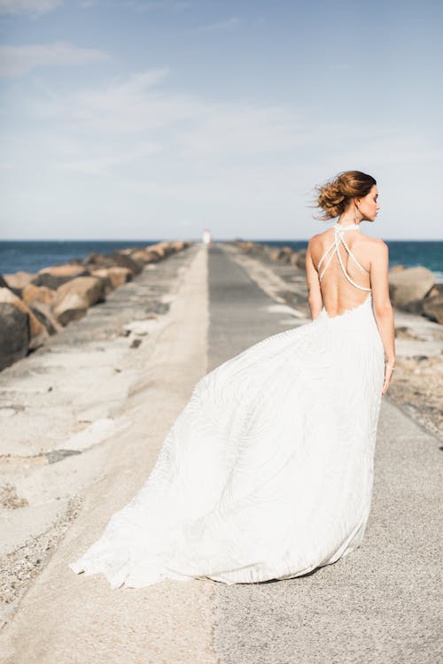 Woman Wearing White Backless Dress Standing On Concrete Boardwalk