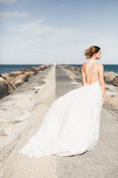 身着优雅婚纱的新娘，站在风景如画的海上码头，晴朗的天空下