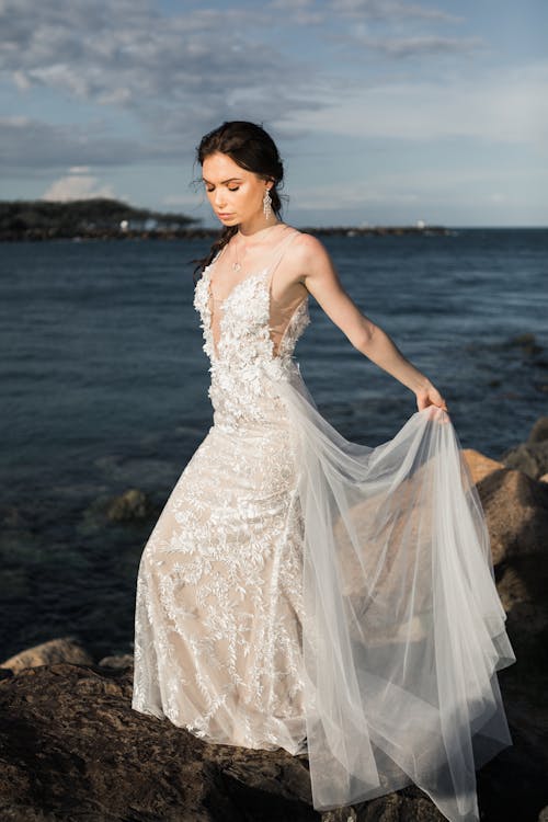 Woman Wearing White Floral Wedding  Dress  Standing On Rocks 