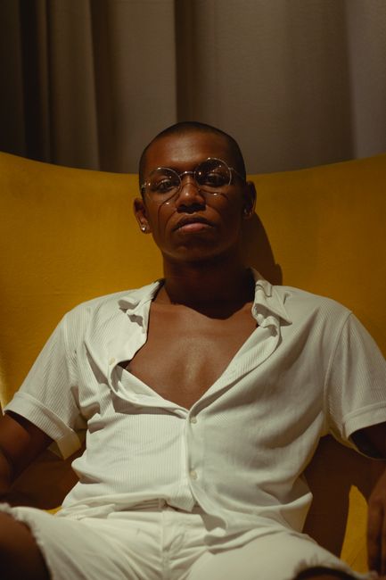 Elegant portrait of a man with eyeglasses sitting on a yellow chair, exuding confidence.