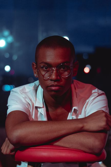 Thoughtful young man with glasses indoors at night, exuding a relaxed yet confident aura.