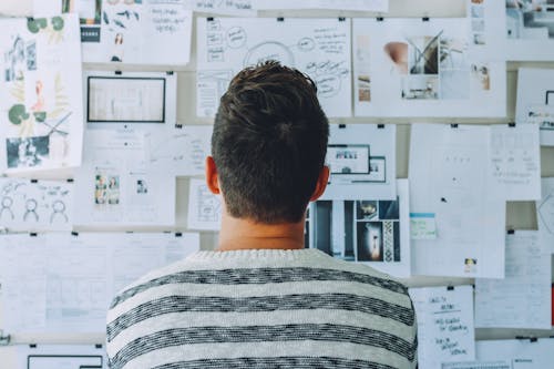 Man Wearing Black and White Stripe Shirt Looking at White Printer Papers on the Wall