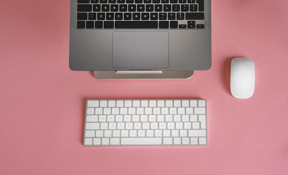 Sleek and modern workspace with laptop and keyboard on pink background for creative inspiration.