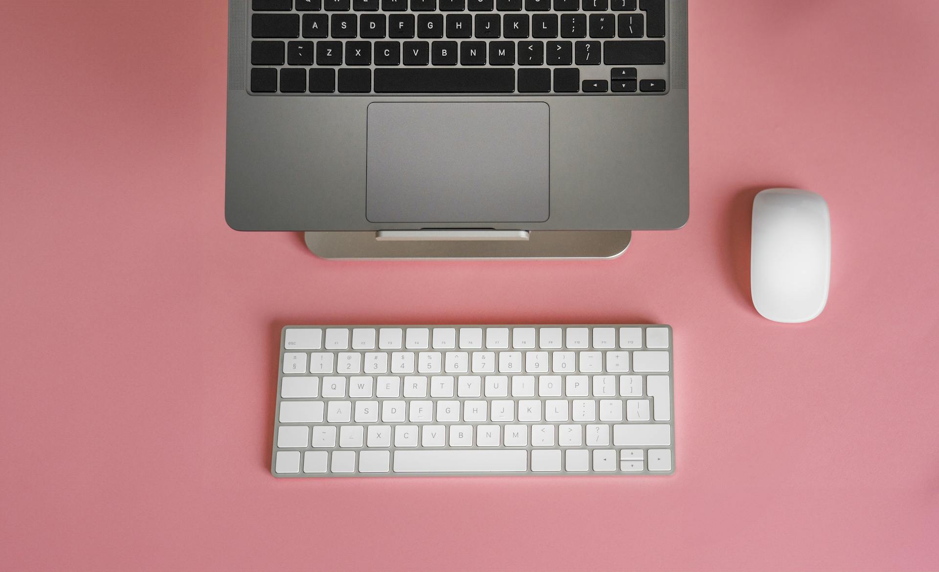 Sleek and modern workspace with laptop and keyboard on pink background for creative inspiration.