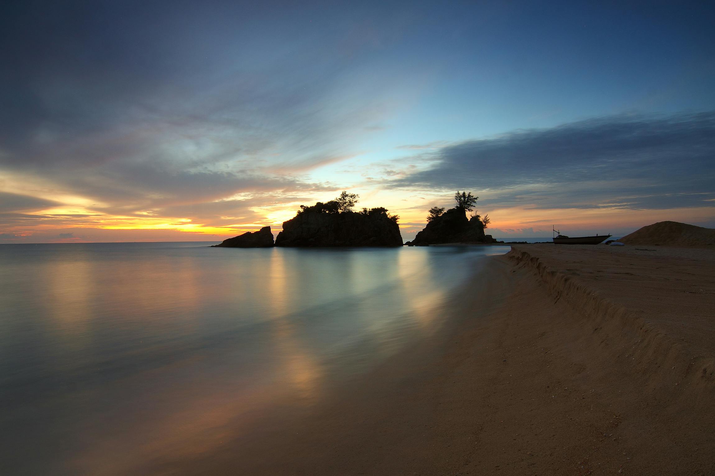 calm body of water near shore with silhouette of rock formation against setting sun