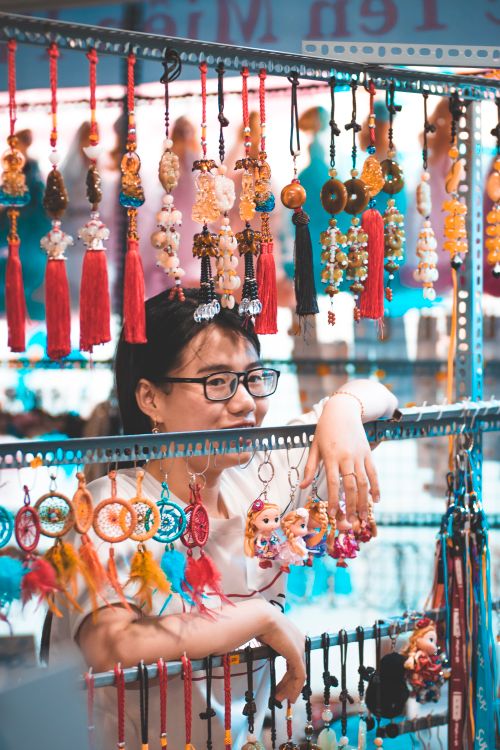 Free Asian woman selling vibrant hanging ornaments at a market stall. Stock Photo