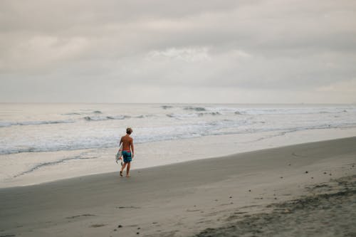 Shirtless Man Holding a Surfboard on Seashore