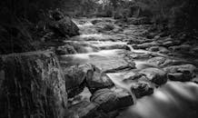 黑白图像中，溪流从岩石上倾泻而下，营造出宁静的自然景观
