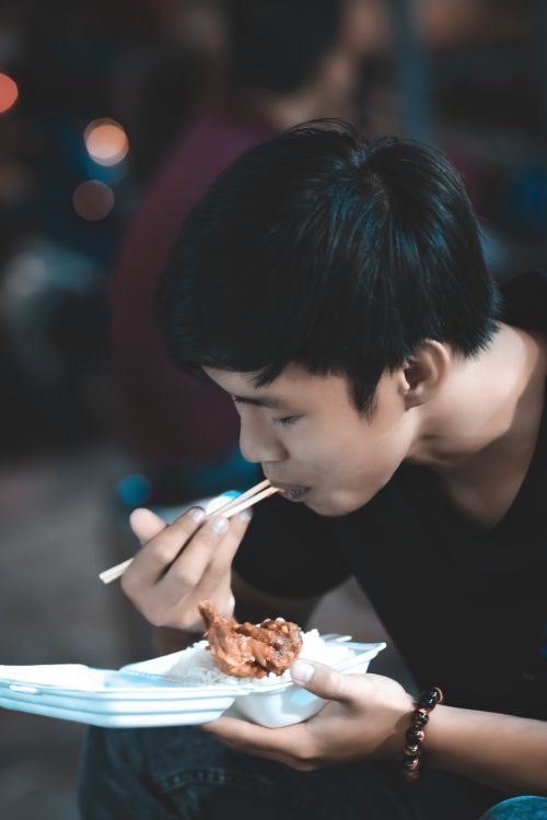 Free A young man savoring a tasty meal with chopsticks in an indoor setting, enjoying the moment happily. Stock Photo