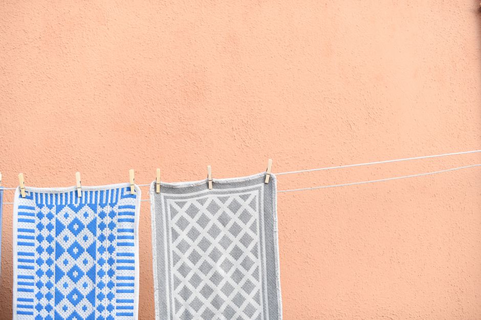 Colorful carpets hanging on a line against a peach wall, showcasing a minimalist pattern contrast.