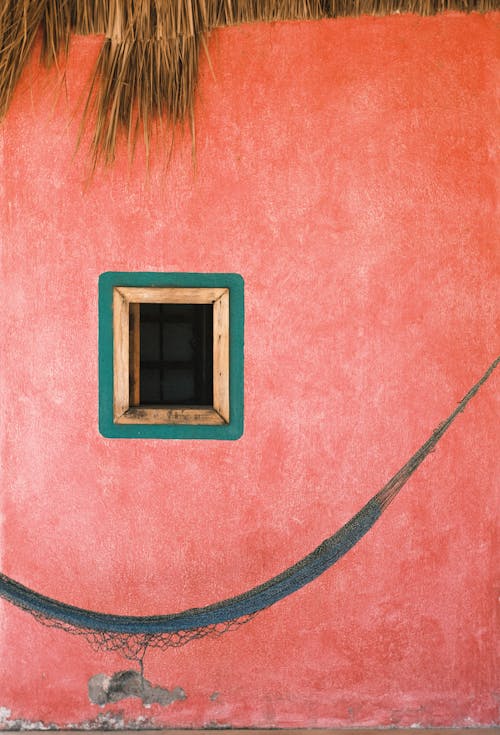 A pink wall with a hammock and a window