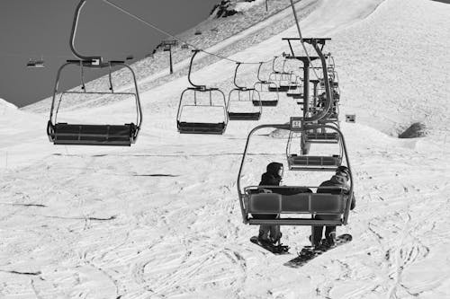 A black and white photo of two people on a ski lift