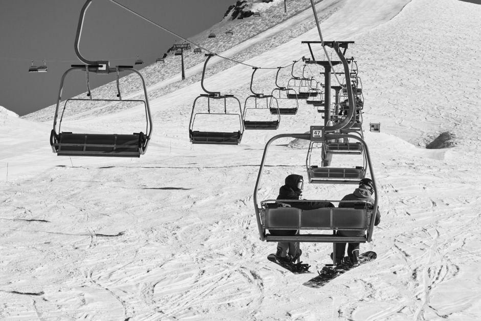 A scenic black and white image capturing people on a ski lift over a snowy slope, perfect for winter sport themes.