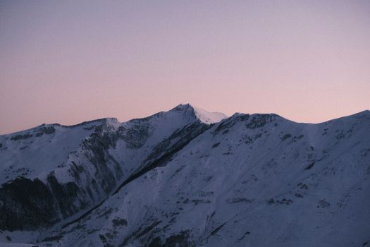 Breathtaking snowy mountain panorama under a pastel dusk sky, capturing winter's serene beauty.