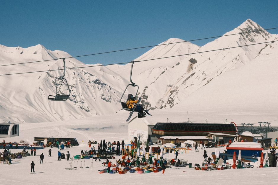 Vibrant ski resort scene with chairlift, snowy mountains, and people enjoying winter sports.