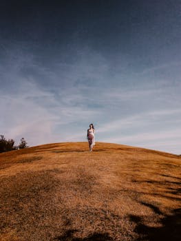 Solitary figure on a windswept grassy hill under a clear sky, evoking solitude and serenity.