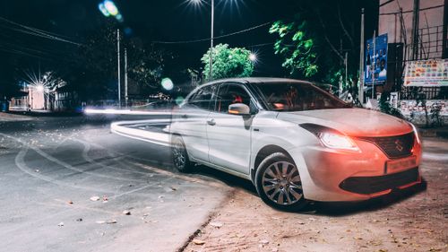 Free A long exposure night shot capturing a parked car and light trails on a city street. Stock Photo