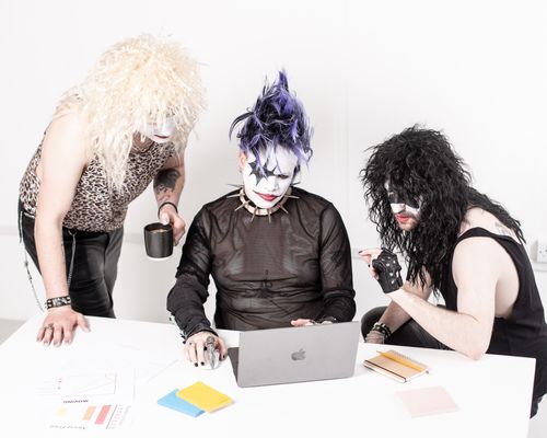 Free Three band members in rock makeup collaborate using a laptop in an office setting. Stock Photo