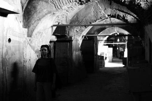 Free A woman walks through a shadowy, arched corridor creating a mysterious atmosphere. Stock Photo
