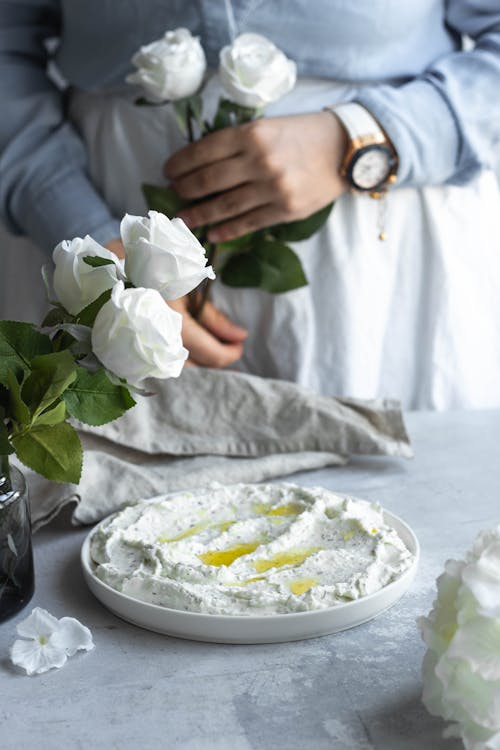 A woman is holding a plate of white flowers and a bowl of cream