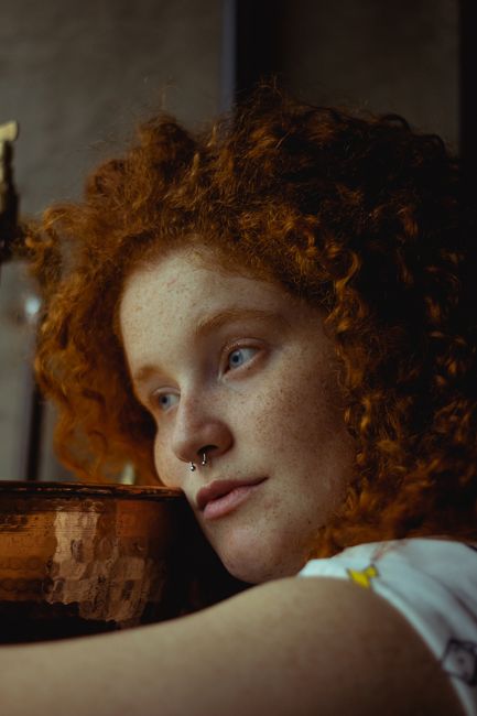 Intimate portrait of a woman with striking curly red hair in soft lighting