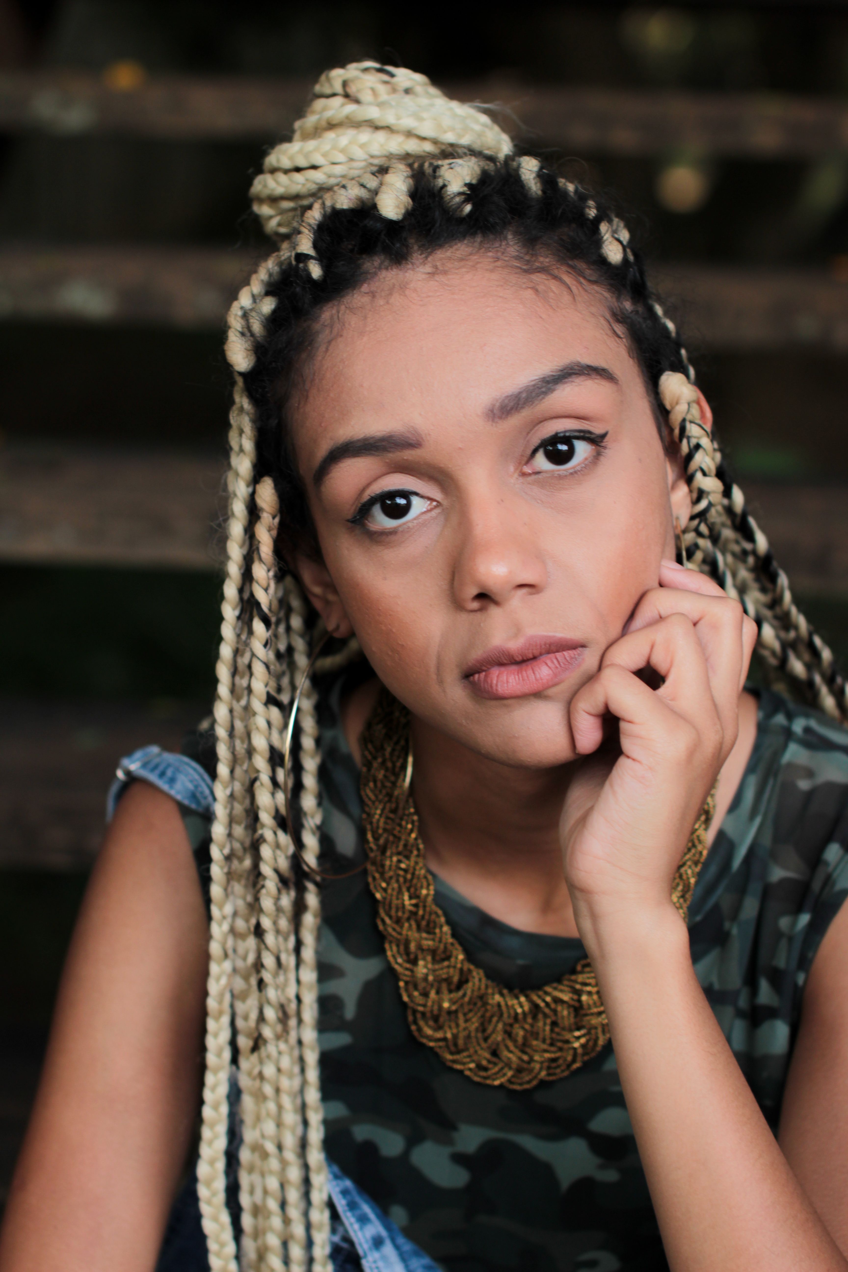 Close-up of a woman with braided hair and a statement necklace, outdoors setting.