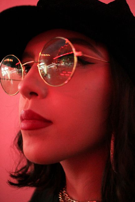 Portrait of a woman in red lighting wearing reflective eyeglasses and lipstick.