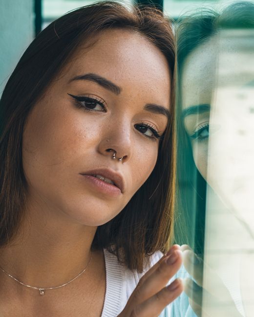 Artistic portrait of a young woman with a glass reflection, showcasing fashion and introspection.