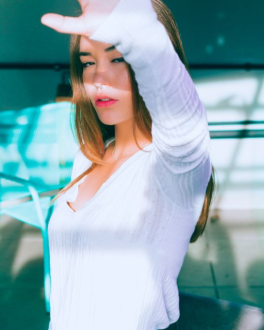 Stylish woman in white blocking sunlight with hand outdoors in urban setting.